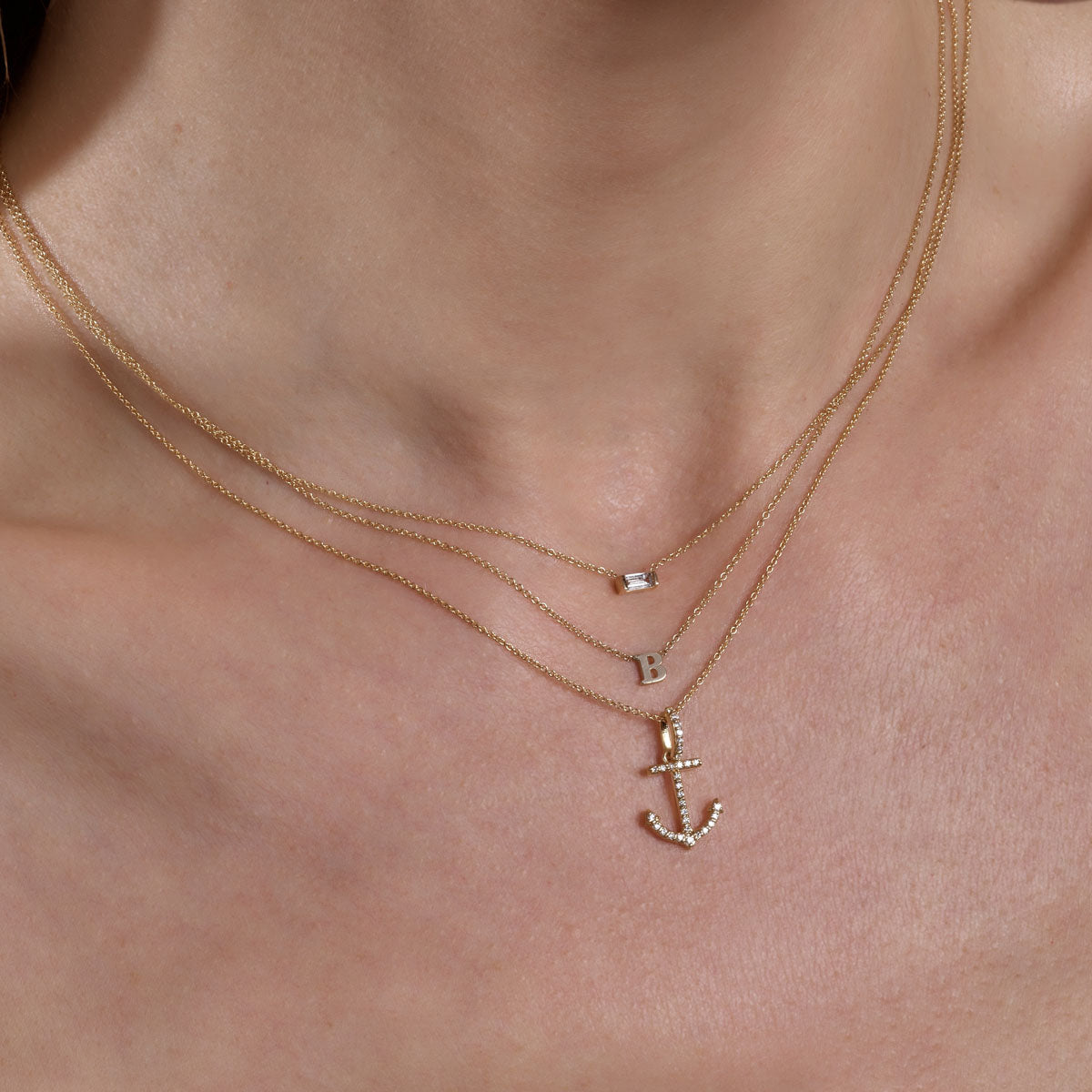 Layered personalized gold necklaces - diamond rectangle, initial, and anchor charms on woman's neck